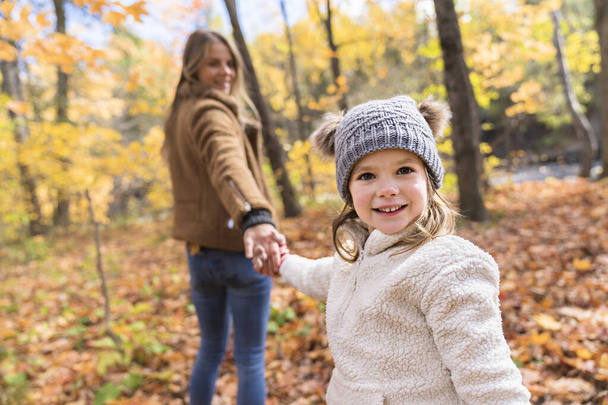 Little girl and her mother playing in the autumn park holding hand - Foto, imagen