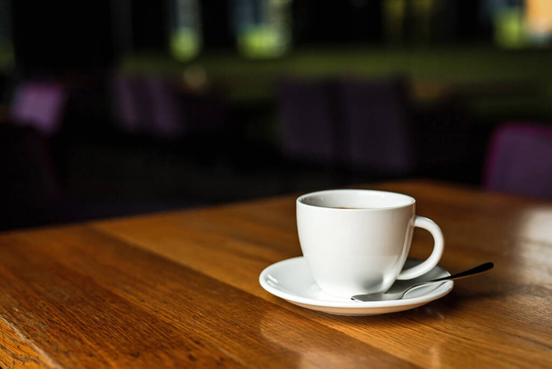 Біла чашка чорної кави, біла тарілка, ложка, дерев'яний стіл, в кафе
 - Фото, зображення