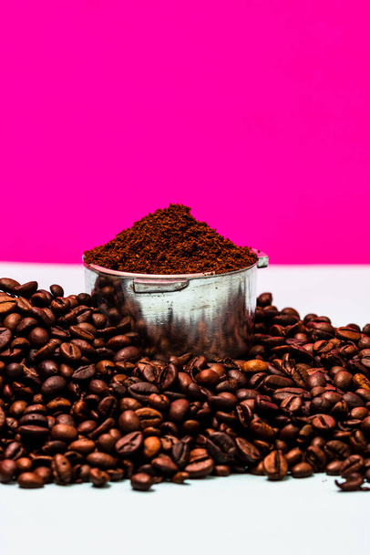 Kaffeebohnen und Portafilter mit gemahlenem Kaffee in einer Komposition auf rosa Hintergrund. - Foto, Bild