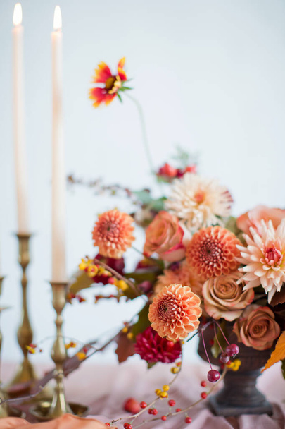 Beautiful flower composition with autumn orange and red flowers and berries. Autumn bouquet in vintage vase on a wooden table with pink tissue and candles - Photo, Image