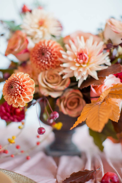Gyönyörű virág összetétele őszi narancs és vörös virágok és bogyók. Őszi csokor vintage vázában egy fa asztalon rózsaszín szövet - Fotó, kép