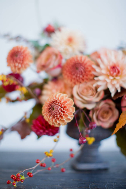 Beautiful flower composition with autumn orange and red flowers and berries. Autumn bouquet in vintage vase on a white wall background - Photo, Image
