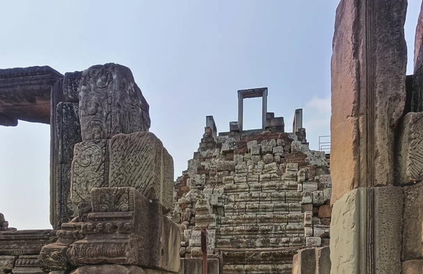 Ruïnes van de oude tempel van Angkor. Op de voorgrond zijn vervallen versierde muren. Verder zijn de trappen naar de top van het kasteel en de open deur tegen de hemel zichtbaar. Cambodja. - Foto, afbeelding