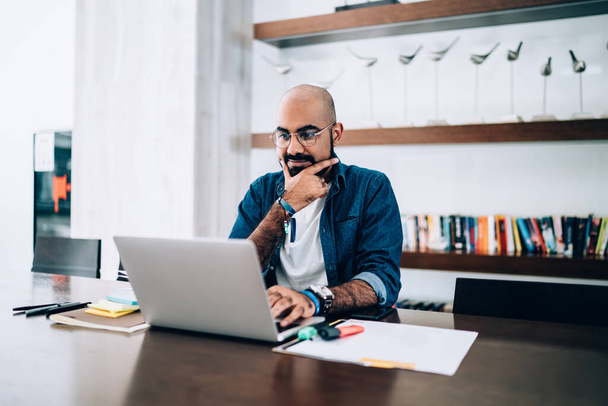 Ближневосточный предприниматель в оптических очках для защиты зрения сидит за рабочим столом офиса с современным ноутбуком и смотрит обучающий вебинар, турецкий бизнесмен просматривает веб-сайт - Фото, изображение