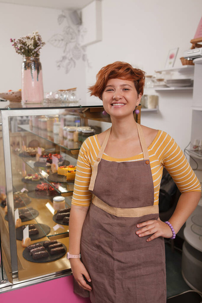 Vertical portrait of a cheerful woman welcoming you at her confectionery store - Photo, Image