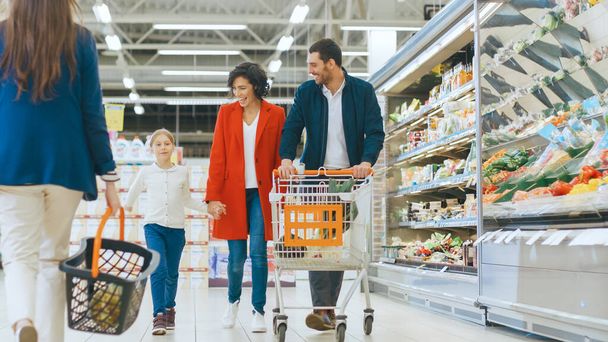 At the Supermarket: Happy Family of Three, Holding Hands, Walks Through Fresh Produce Section of the Store. Father, Mother and Daughter Having Fun Time Shopping. - Photo, image