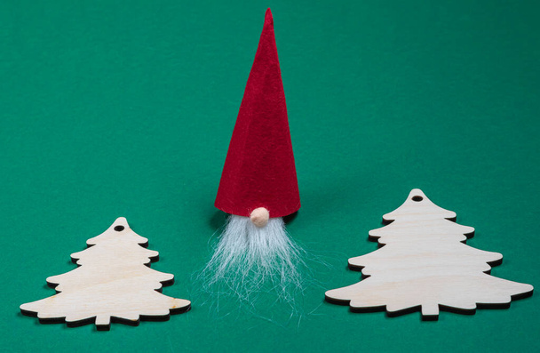 Domácí vánoční řemeslné dekorace.Červený trpaslík a dřevěný vánoční stromeček na zeleném pozadí - Fotografie, Obrázek