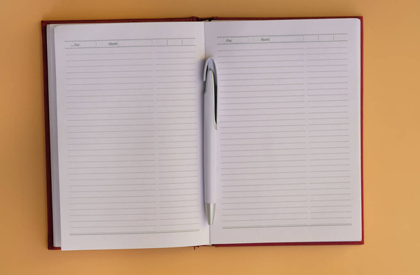 Notepad with horizontal lines on a yellow background top view. Notebook with white pen. Blank sheets of notebook. Diary with a red cover for the to-do list of the day. - Photo, Image