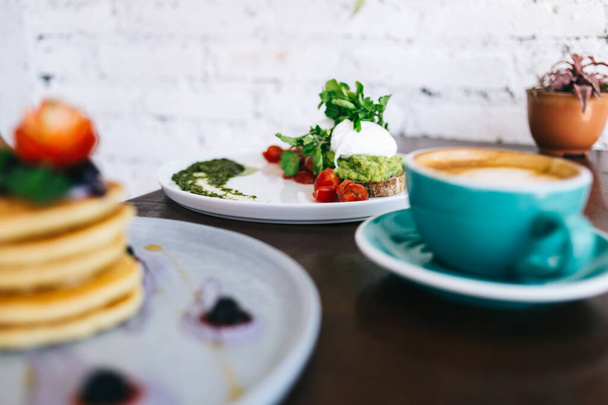 Conjunto de desayuno con huevo escalfado en pan y postre de panqueques con bayas colocadas en la mesa cerca de la taza azul de café - Foto, imagen