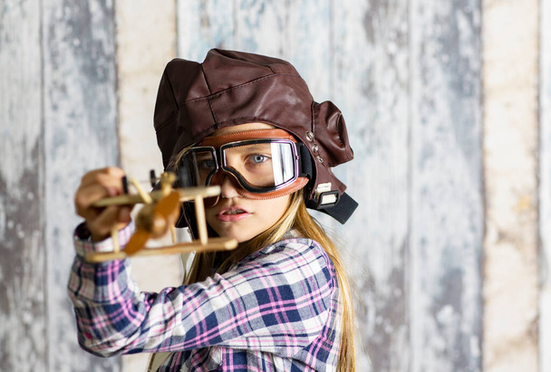 κορίτσι πιλοτικό καπέλο και γυαλιά με ξύλινο αεροπλάνο - Φωτογραφία, εικόνα