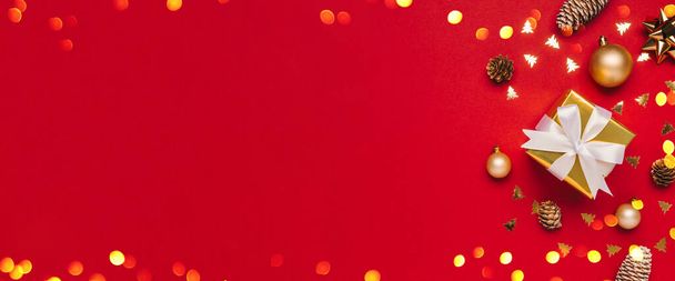 Feliz Navidad y Felices Fiestas tarjeta de felicitación de fondo con copyspace a la izquierda. Regalos de Navidad, luces bokeh y decoración dorada sobre fondo rojo vista superior. Tema de vacaciones de Navidad de invierno en planas - Foto, imagen