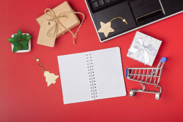 Laptop, notebook, shopping cart and boxes on a bright red background. Online shopping concept - Foto, Imagem