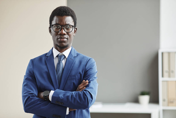 Portrait d'un jeune homme d'affaires africain portant des lunettes et des vêtements de cérémonie, les bras croisés et regardant la caméra - Photo, image