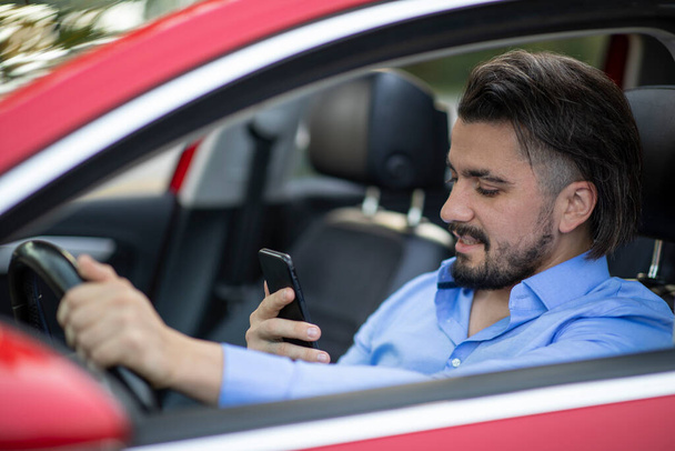 Handsome young man looking at the phone while driving and smiling - Foto, immagini