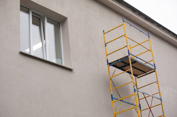 Reparación y renovación exterior de una casa de apartamentos utilizando una pequeña torre de andamios de metal de pintura azul. Esquina de un edificio de apartamentos típico urbano con andamios cerca - Foto, Imagen