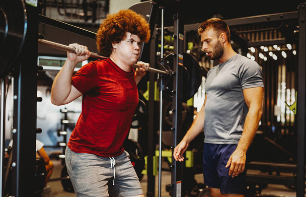 Overweight young chubby man exercising gym with personal trainer - Foto, Imagem