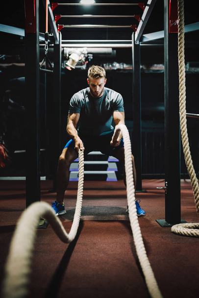 Happy fit man working out with battle ropes at fitness gym - 写真・画像