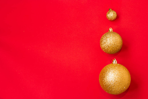 Three golden Christmas balls of different sizes are displayed in a row as a border on a red background. New Year mood mok up. Copy space - Foto, afbeelding