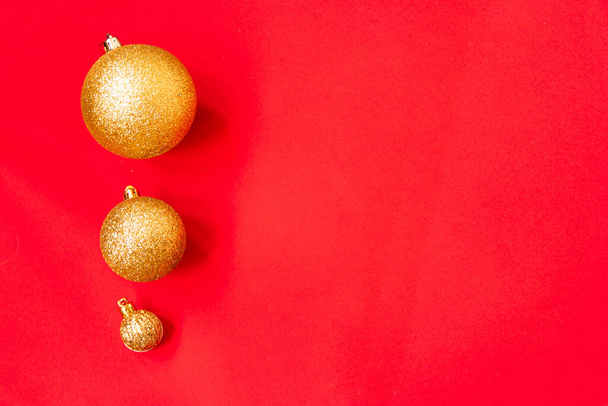 Three golden Christmas balls of different sizes are displayed in a row as a border on a red background. New Year mood mok up. Copy space - Φωτογραφία, εικόνα