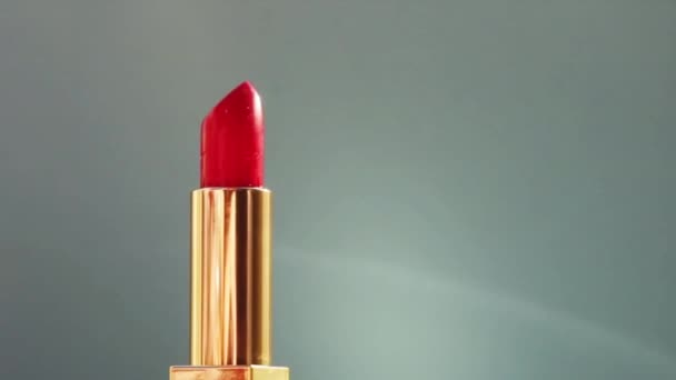 Luxusní červená rtěnka ve zlaté tubě na barevném pozadí a zářící světelné erupce, luxusní make-up a rekreační kosmetika pro krásu značky - Záběry, video