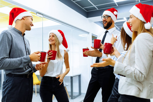 Group of happy business people wearing Santa Claus hats talking and smiling while celebrating New Year in the office. New Year and Merry Christmas - Foto, imagen