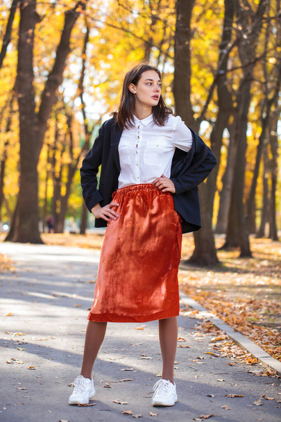 Full body portrait of a young brunette woman in orange skirt walking in autumn park - Фото, зображення