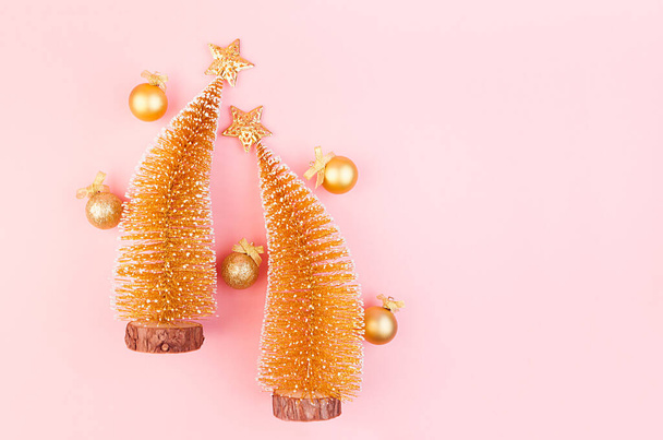 Golden christmas decorations with christmas trees, stars, balls on soft light pink background, copy space, top view. - 写真・画像