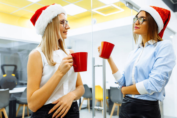young business women in santa claus hats drinking tea or coffee during office break - Фото, зображення