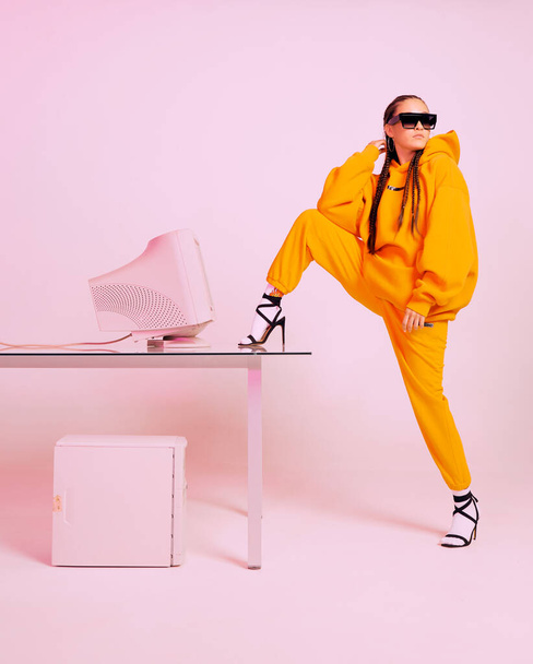 Stylish girl office worker in sunglasses with obsolete computer and foot on desk. Colored Neon light - Фото, зображення