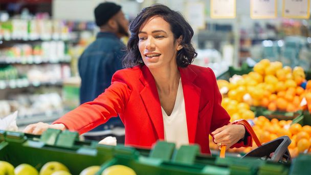 At the Supermarket: Portrait of the Beautiful Smiling Woman Choosing Organic Fruits In the Fresh Produce Aisle and Puts them into Shopping Basket. - Foto, imagen