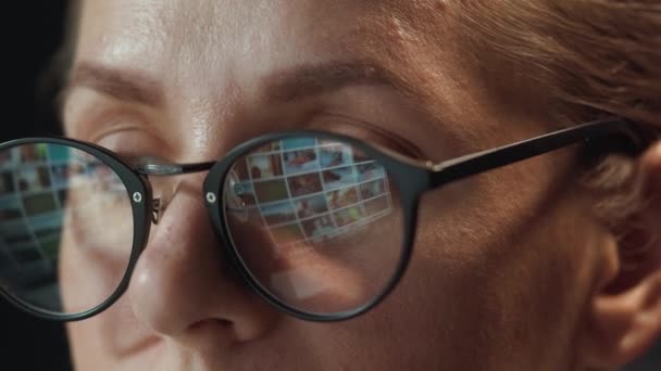 Egy szemüveges nő nézi a monitort és szörfözik az interneten. A monitor képernyője tükröződik a szemüvegben. Éjszaka dolgozom. Belügyminisztérium. Távoli munka - Felvétel, videó