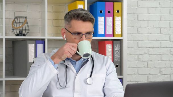 Doktor hastayı internetten dinliyor. Bilgisayarı arıyor. Web kamerası, kahve çayı içiyor. - Fotoğraf, Görsel