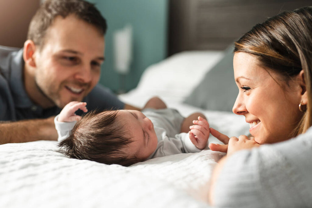 A beautiful couple with newborn Baby on bed. - Zdjęcie, obraz
