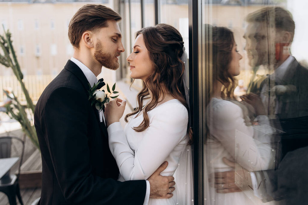 Stylish european wedding couple hugging and looking at each other. Portrait of a cute newly married couple. The bride is dressed in a white wedding dress with veil. Groom dressed in a black suit. - Photo, image