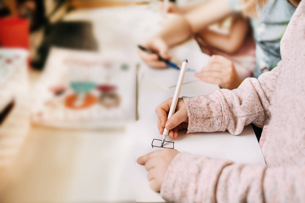 Erkek kardeşinin yanında oturan küçük bir kız öğrenim sırasında elinde keçeli kalem ve kalemle kağıda resim çiziyor..  - Fotoğraf, Görsel