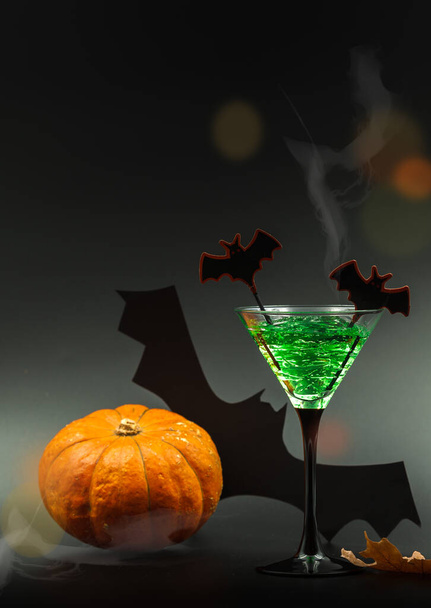 Green cocktail for a Halloween party with decorative bats and pumpkins. On a black background with smoke and light spots - Photo, Image