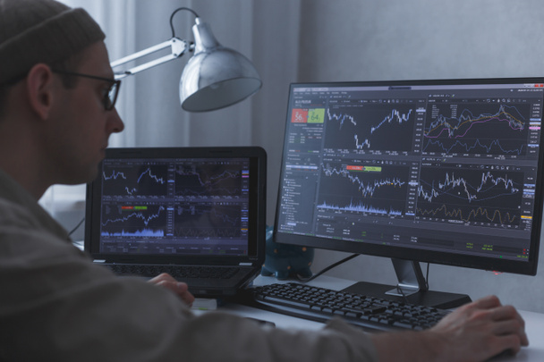 Продуманный серьезный брокер, анализирующий графики фондового рынка на ПК и ноутбуке - Фото, изображение