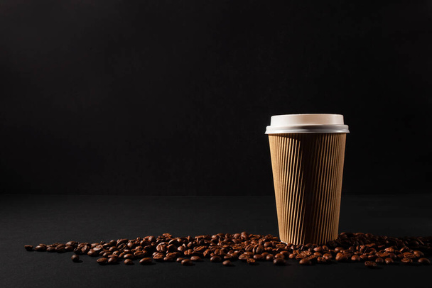 Paper cup of coffee with coffee beans on black background. Side view. Take away cup. Horizontal orientation. - Fotografie, Obrázek