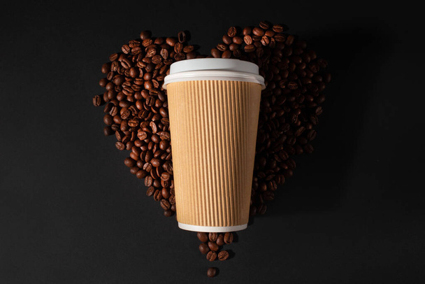 Paper cup of coffee with coffee beans on black background. Top view. Coffee lovers. - 写真・画像