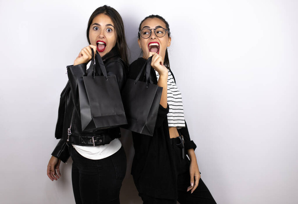 zwei junge schöne Frauen mit einer schwarzen Einkaufstasche überrascht. Schwarzer Freitag - Foto, Bild