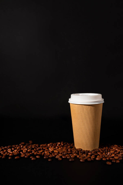 黒を背景にコーヒー豆とコーヒーの紙コップ。サイドビュー。コップを取りなさい。垂直方向. - 写真・画像