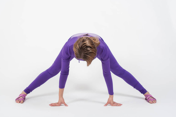 Kaunis nainen violetti säärystimet ja top tekee liikuntaa venyttely valkoisella pohjalla. Alaston meikki - Valokuva, kuva