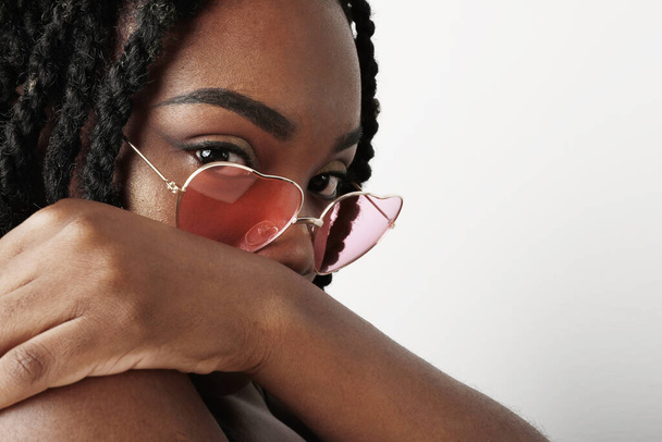 Close-up portrait of black woman, wearing pink glasses posing over white background. Skin care concept. - Foto, Bild