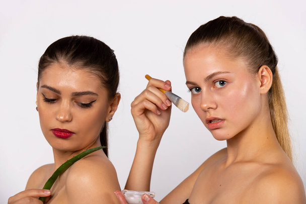 Two young, attractive girls prefer natural products for facial skin care. Spa and beauty concept. Photo on white background - Fotó, kép