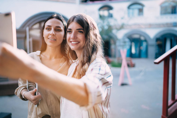 Happy Caucasian bloggers smiling at front smartphone camera while making selfie content for network sharing, cheerful millennial hipsters using modern technology for photographing outdoors - Фото, зображення