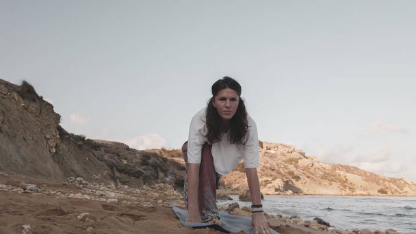 jong Kaukasisch brunette vrouw doen youga op het zandstrand in de ochtend - Foto, afbeelding