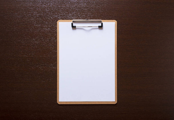 Un portapapeles de madera con papel blanco, colocado sobre un fondo de madera - Foto, Imagen