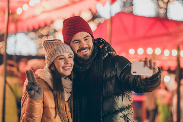 Two people students friends take selfie on cellphone girl make v-sign on outdoors x-mas christmas town event - Photo, Image