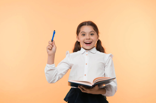 Girl cute schoolgirl in uniform hold book or textbook yellow background. Diligent pupil get knowledge from book. Child wear school uniform prepare for lesson her knowledge. Excited about knowledge - Fotoğraf, Görsel