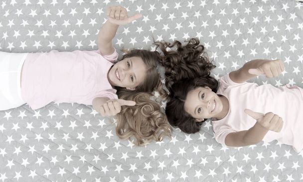 Kids show thumbs up gesture. Girls children on bed top view. Pajamas party concept. Girls just want to have fun. Girlish secrets honest and sincere. Friends have nice time pleasant leisure - Foto, afbeelding